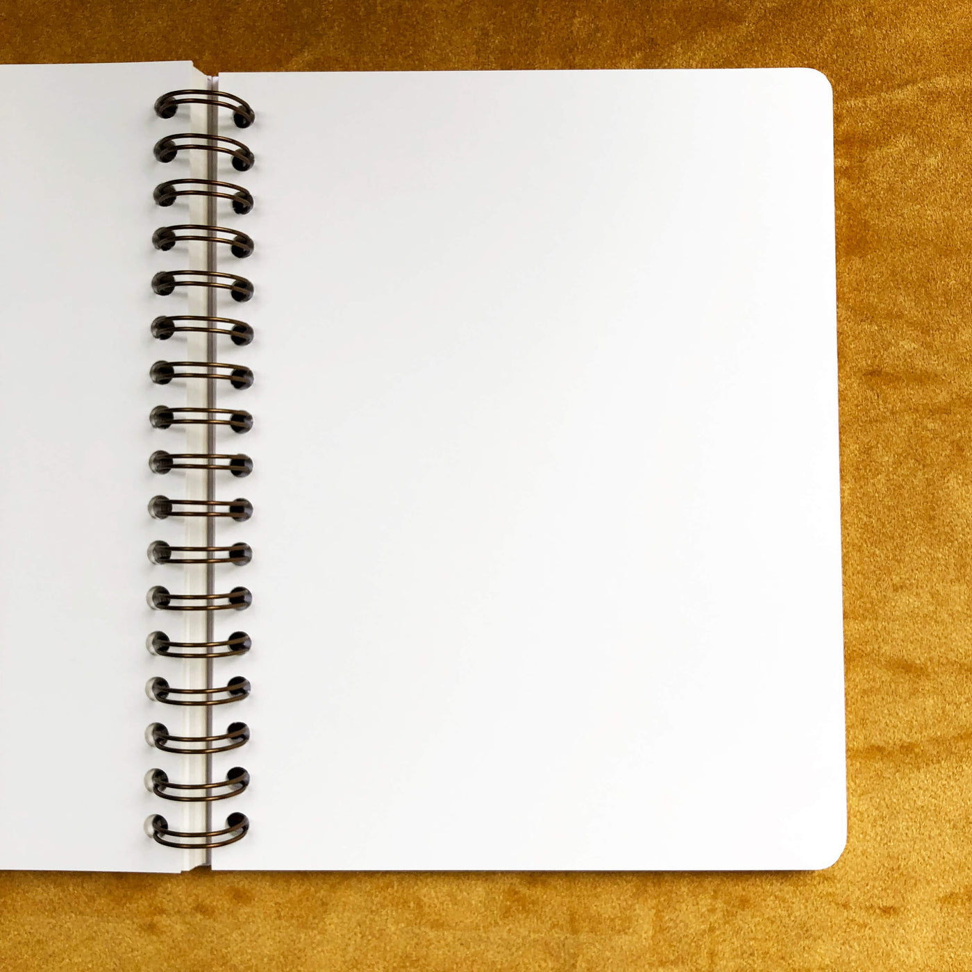 Open notebook with blank pages and spiral binding on a golden yellow velvet background