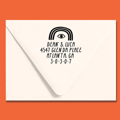 White envelope with black eye and rainbow arch address stamp on an orange background